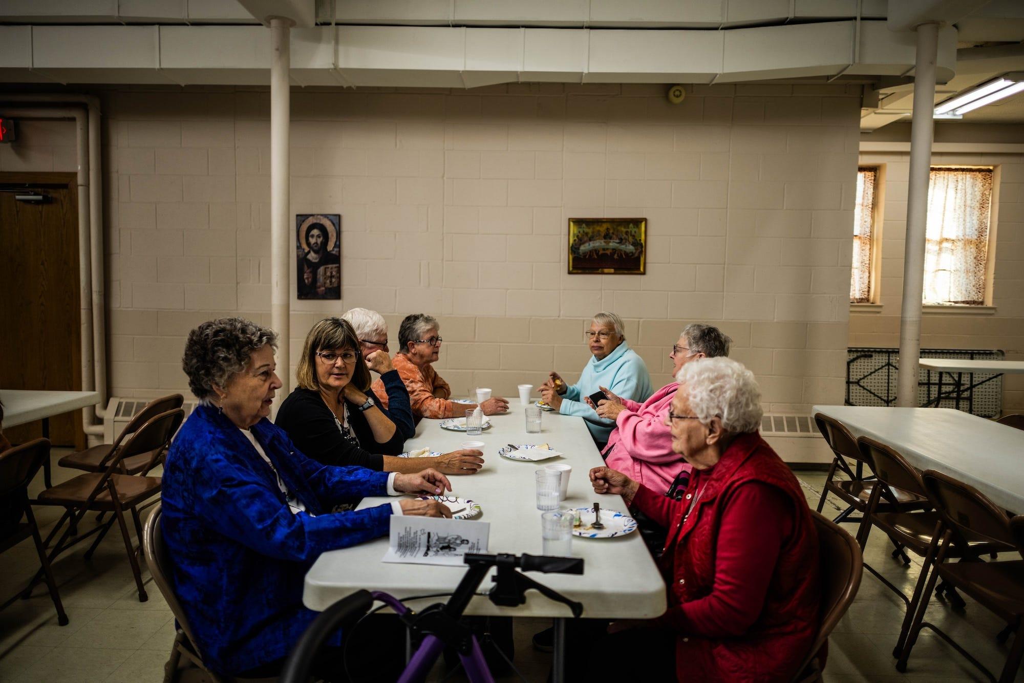 un groupe de personnes âgées est assis autour d'une table, chacun avec des assiettes de desserts et des tasses de boissons