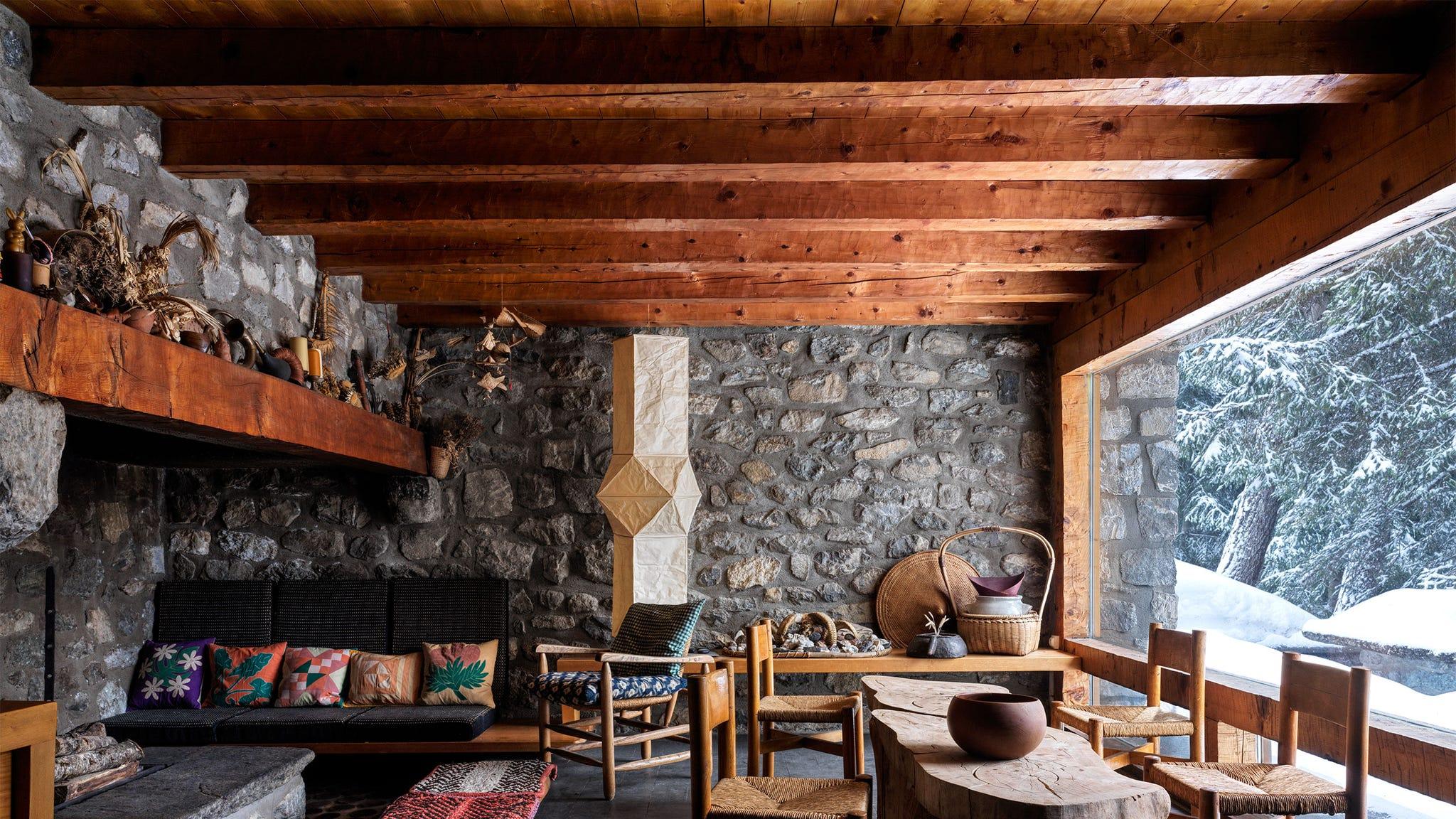 une pièce avec une cheminée et des chaises et un plafond à poutres et des murs en pierre grise ornée de galets